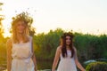 Two girlfriends, young girls in white dresses and flower wreaths on their heads, standing in a river of water, near the shore, Royalty Free Stock Photo