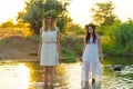 Two girlfriends, young girls in white dresses and flower wreaths on their heads, standing in a river of water, near the shore, Royalty Free Stock Photo