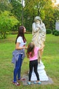 Two girls admire the monument in park. Girls looking at statue