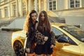 Two girls on a background of a yellow car. Beautiful brunettes near the cottage arrived on an expensive car. Famous girls.