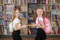 Two girls with backpacks meet and exchange books in school library. Benefits of everyday reading