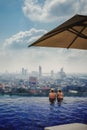 Two Girls in Bikinis Swimming in Infinity Pool Overlooking Bangkok Thailand Urban City Landscape Luxurious Vacation Destination