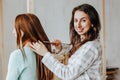 Two girls braid their hair at the window. Woman makes a braid to her friend. Hair weaving hairstyles. Girlfriend braids her hands Royalty Free Stock Photo