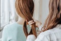 Two girls braid their hair at the window. Woman makes a braid to her friend. Hair weaving hairstyles. Girlfriend braids her hands Royalty Free Stock Photo