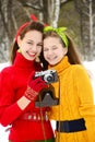 Two girls in bright multi-colored sweaters laugh merrily and hold an old camera in their hands against the background of a winter Royalty Free Stock Photo