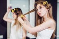 Two girls curling their hair with rollers in a room