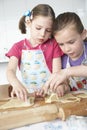 Two girls (5-6) cutting dough in kitchen