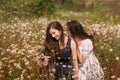 Two girls in dark blue and white dresses in sunny day sitting in chamomile field Royalty Free Stock Photo