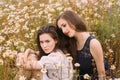 Two girls in dark blue and white dresses in sunny day sitting in chamomile field Royalty Free Stock Photo