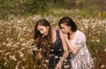 Two girls in dark blue and white dresses in sunny day sitting in chamomile field Royalty Free Stock Photo