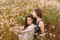Two girls in dark blue and white dresses in sunny day sitting in chamomile field Royalty Free Stock Photo