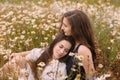 Two girls in dark blue and white dresses in sunny day sitting in chamomile field Royalty Free Stock Photo