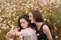 Two girls in dark blue and white dresses in sunny day sitting in chamomile field Royalty Free Stock Photo