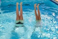 Two girls are doing handstand in a swimming pool in the summer