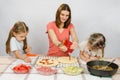 Two girls enthusiastically watched as mum pours ketchup basis for pizza