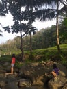 Yogyakarta, Indonesia- June, 2021: Two girls are fishing in the river with rice fields and big trees in the background. Royalty Free Stock Photo