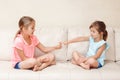 Two girls friends playing rock paper scissors hand game. Caucasian children sitting on a couch playing together. Interesting Royalty Free Stock Photo