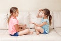 Two girls friends playing rock paper scissors hand game. Caucasian children sitting on a couch playing together. Interesting Royalty Free Stock Photo
