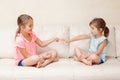 Two girls friends playing rock paper scissors hand game. Caucasian children sitting on a couch playing together. Interesting Royalty Free Stock Photo