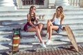 Two girls girlfriends, sitting on the stairs in summer in the city, talking talk, happy laugh and smile, skateboard Royalty Free Stock Photo