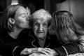 Two girls granddaughter kissing the cheeks of his old grandmother.