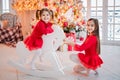 Two girls have fun riding toy horse in front of a Christmas tree Royalty Free Stock Photo