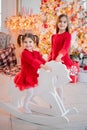 Two girls have fun riding toy horse in front of a Christmas tree Royalty Free Stock Photo