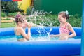 Two girls have fun splashing in an inflatable pool on a summer day in the backyard Royalty Free Stock Photo