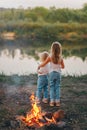 Two girls holding hands and standing back on bank of river and admire on sunset Royalty Free Stock Photo