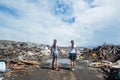 Two girls holding hands standing on the muddy road facing garbage dump