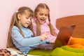 Two girls include laptop at work, sitting on bed Royalty Free Stock Photo