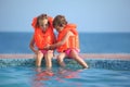 Two girls in lifejackets sitting on ledge pool