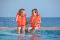 Two girls in lifejackets sitting on ledge pool Royalty Free Stock Photo