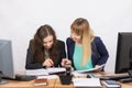 Two girls are looking for colleagues sitting together the right information at the same table in the office Royalty Free Stock Photo