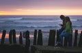 Two girls looking down at cell phone by sea shore at sunset Royalty Free Stock Photo