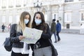 Two girls looking at a tourist map on the street. They are wearing face masks