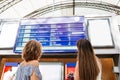 Two women looking at train schedule hanging at wall