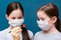 Two girls in medical masks are examining a coronavirus which one of them holds in tweezers. Hand in latex glove.