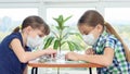 Two girls in medical masks sit at a table and play board games