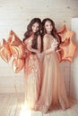 Two Girls on party. Beautiful young women in elegant golden dress with champagne glasses over golden star balloons background. H Royalty Free Stock Photo