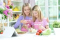 Two girls in pink aprons pouring oil in salad