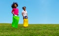 Two girls play gunny sack race jumping downhill