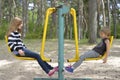 Two girls are playing on the playground on the yellow metal attraction. It's windy.