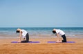 Women practicing camel yoga pose on the beach