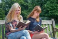 Two girls reading books on bench in nature Royalty Free Stock Photo