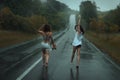 Two girls are on roadway in the rain.