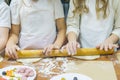 Two girls roll out two pieces of dough with one rolling pin on wooden pizza table.