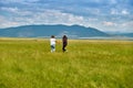 Two girls run through the green grass of the Barguzin Valley in the Republic of Buryatia. View from the back.