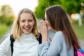 Two girls schoolgirl. In summer in park in nature. Teenagers communicate on street. Tell each other in ear. The concept Royalty Free Stock Photo