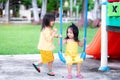 Two girls share swing. The eldest is teaching the youngest sister to swing the blue swing. Pretty kid girls intimate and play